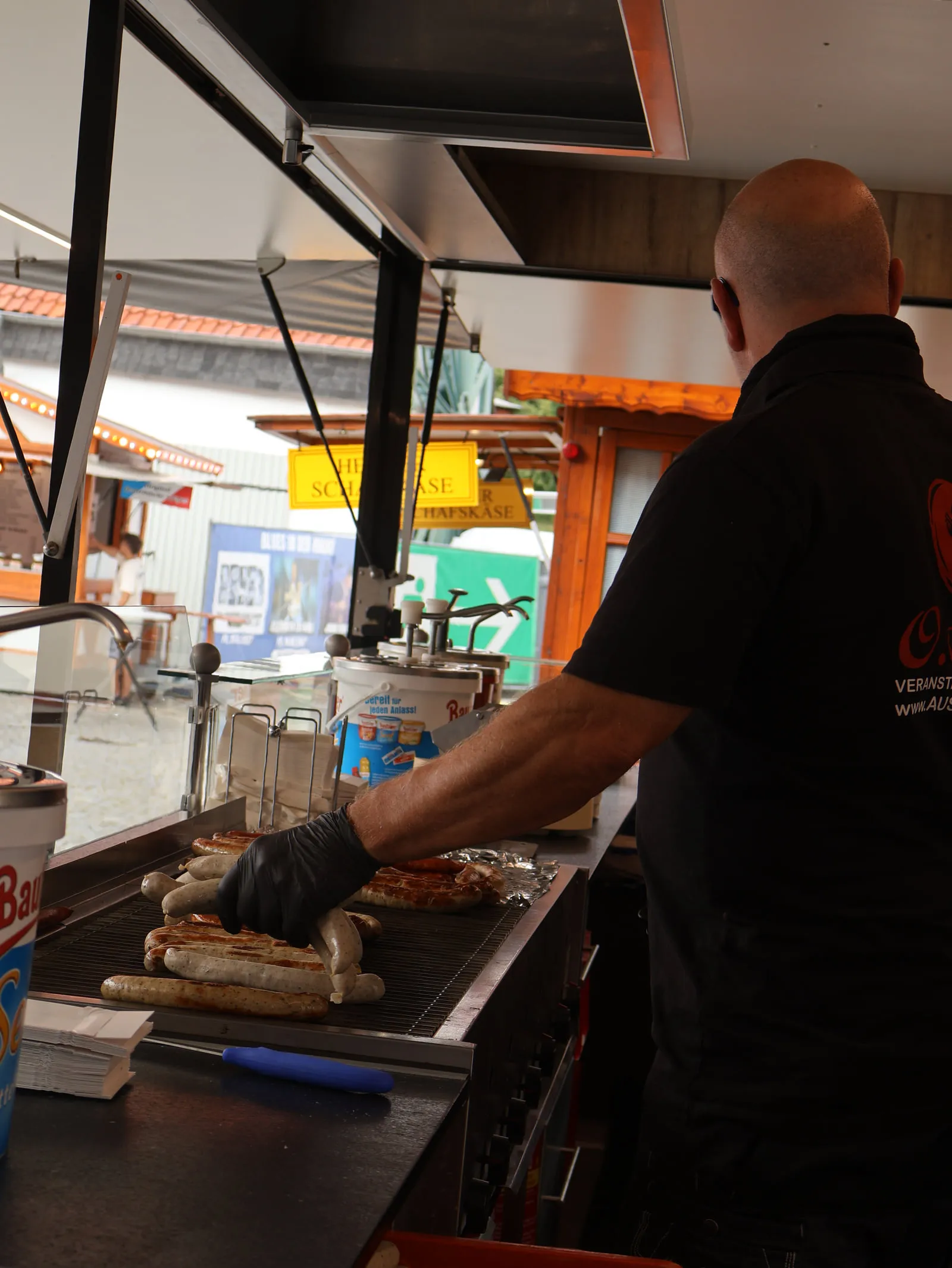 Mitarbeiter von Aust Catering legt Bratwürste auf den Grill im Cateringwagen