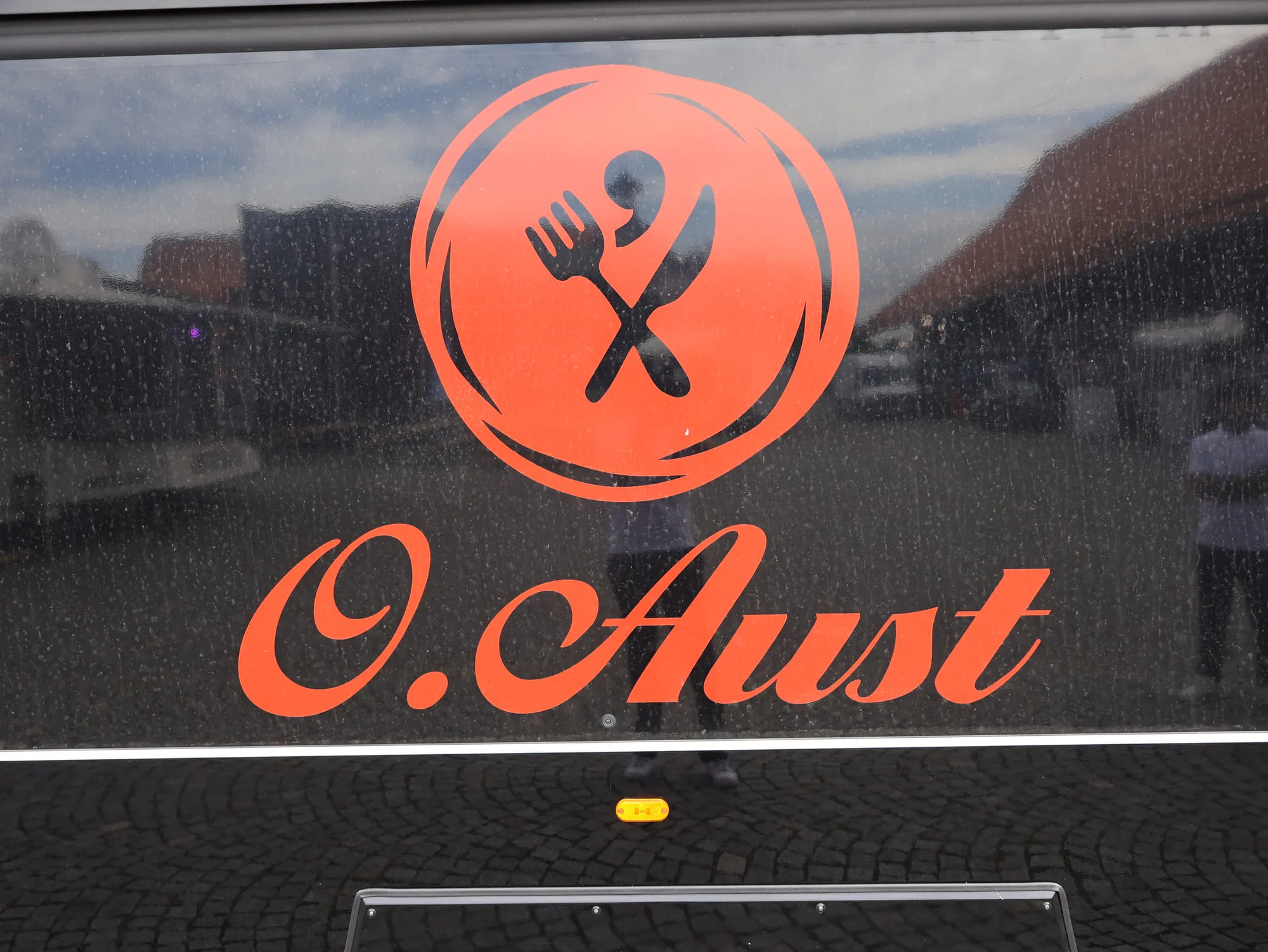 Nahaufnahme des O. Aust Schriftzugs auf der schwarz lackierten Seitenwand des Cateringwagens