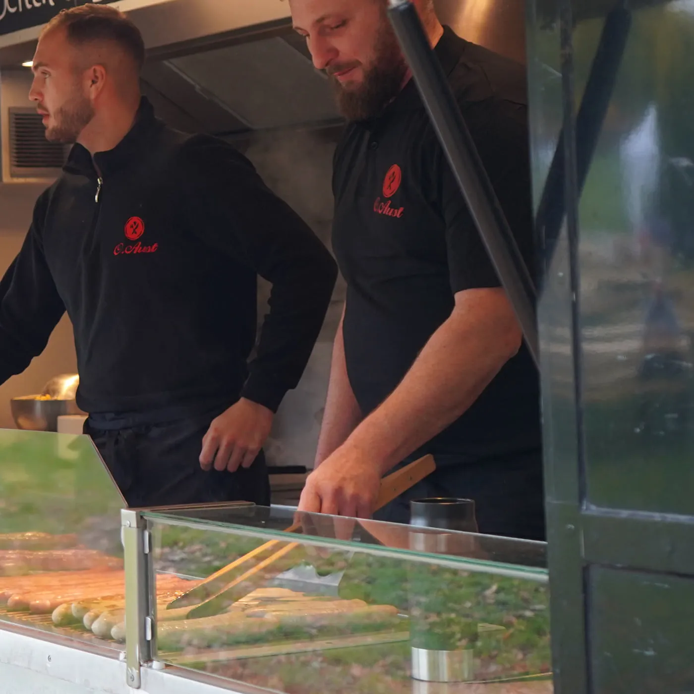 Zwei Mitarbeiter von Aust Catering am Grill im kleinen Cateringwagen